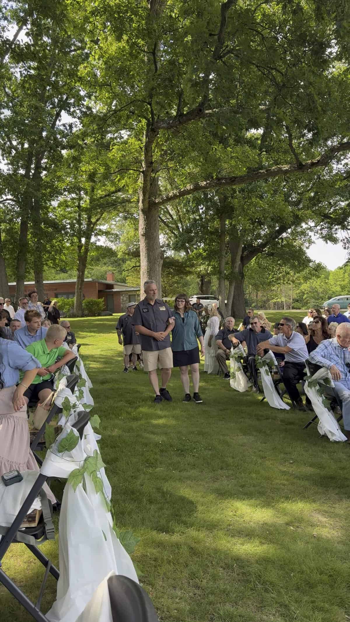 Guests attending outdoor wedding ceremony under large tree at Camp Happily Ever Af.