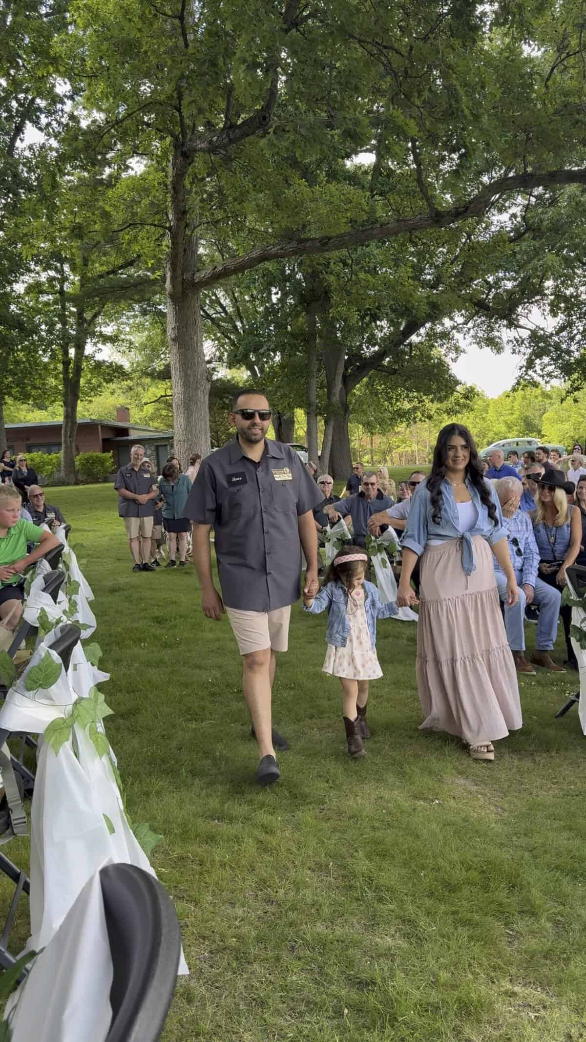 Family walking outdoors at Camp Happily Ever After event with trees and crowd.